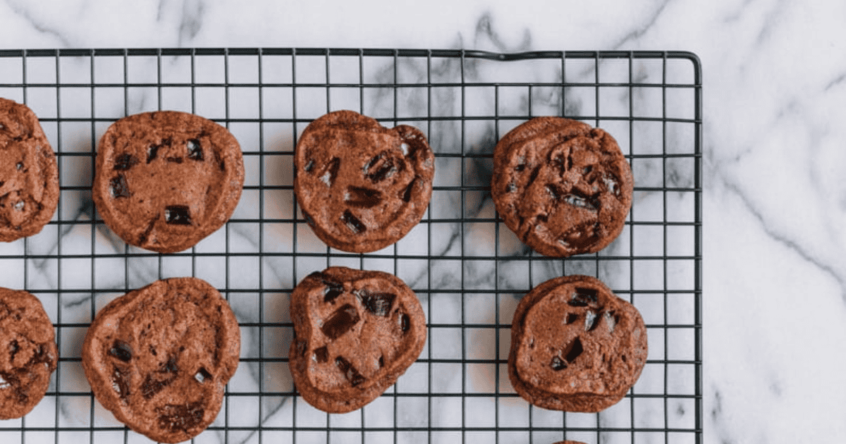 A wire cooling rack holds several chocolate cookies with chocolate chunks on a white marble surface—perfect for enjoying mindfully or as a comforting treat when considering what to do after a binge.