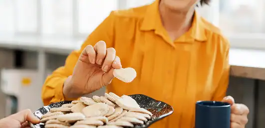 Person in yellow shirt holding a blue mug and taking a round cracker from a black plate filled with similar crackers.